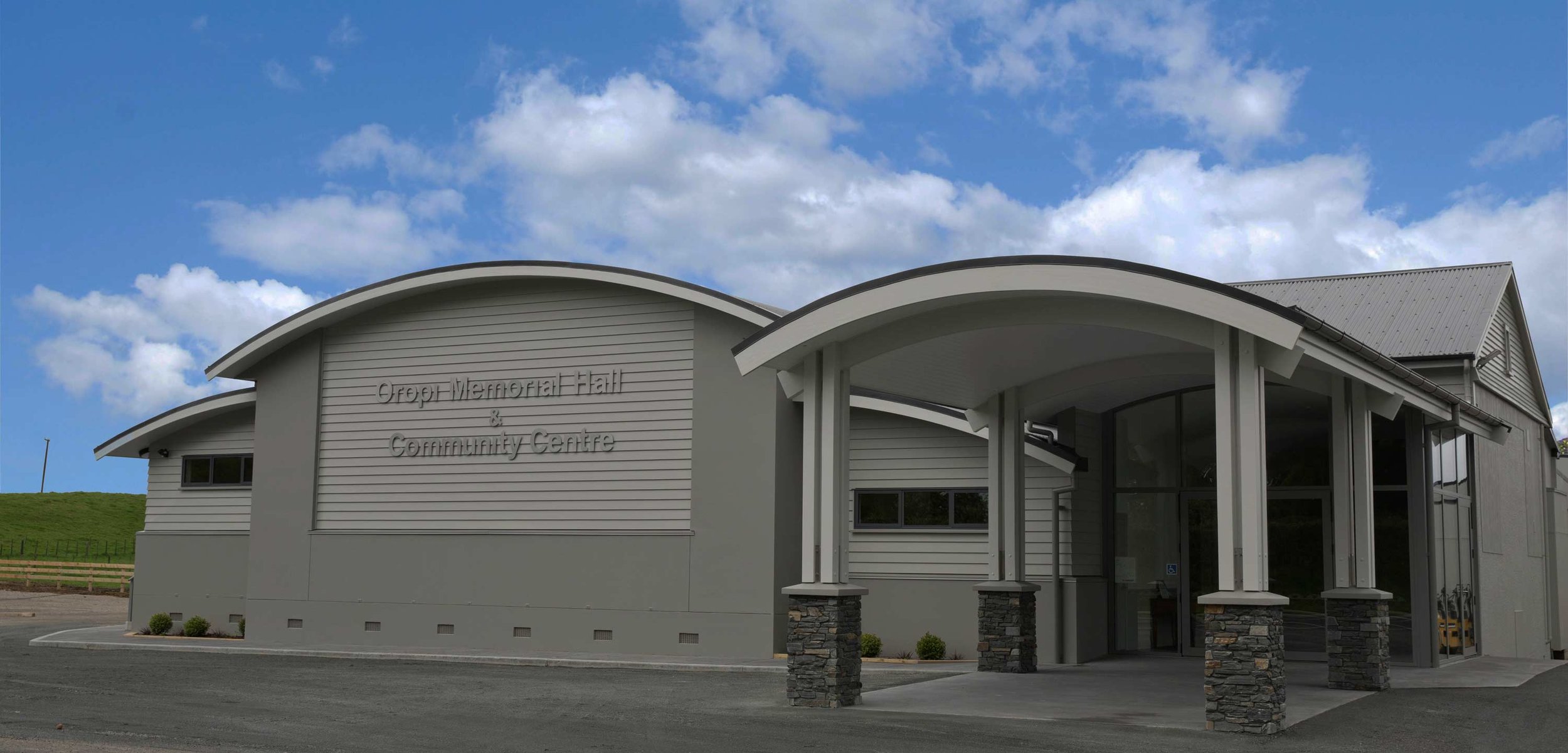Contemporary curved-roof community hall with stone-clad entrance columns and signage