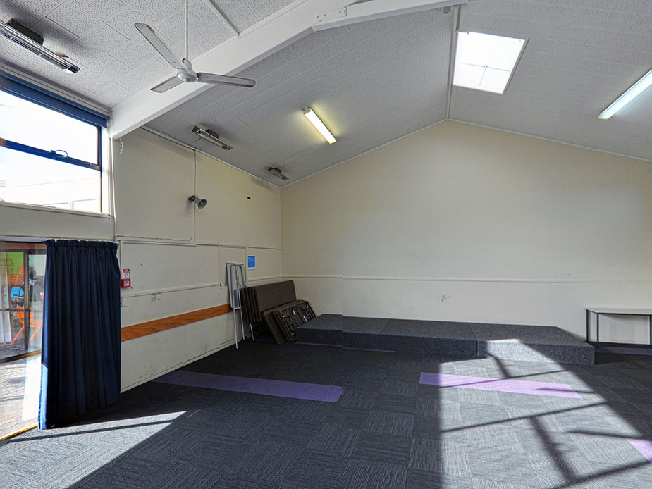 Plain hall with carpeted floor, yoga mats, and folded tables stored against wall