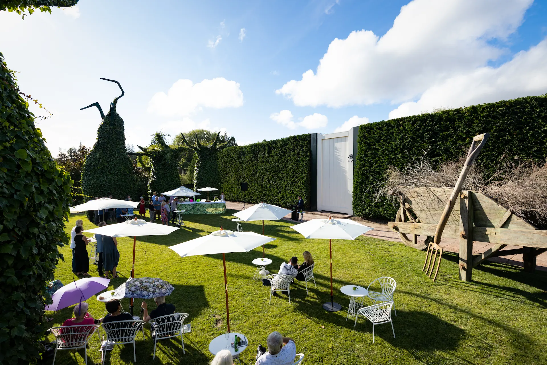 Garden courtyard set for outdoor event with white market umbrellas and sculptural elements