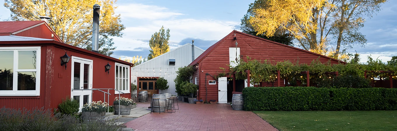 Red painted timber buildings with a courtyard, barrel planters, and autumn trees