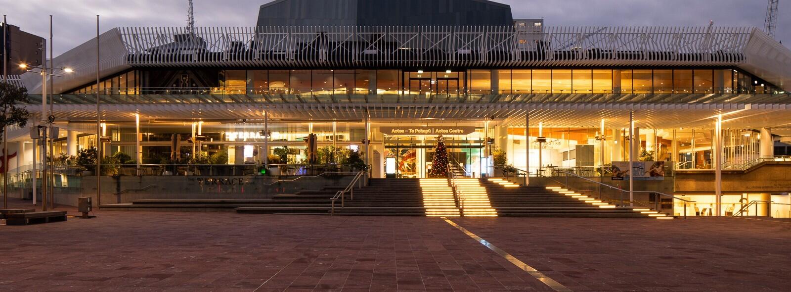 Large civic building exterior at dusk with illuminated entrance and plaza