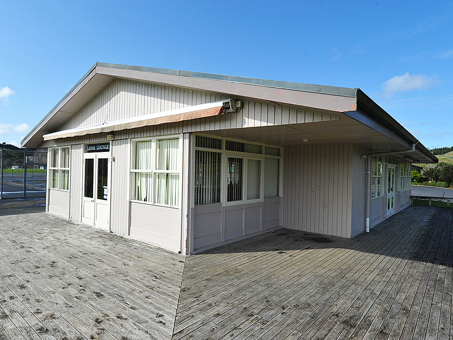 Single-storey weatherboard lounge building with deck on grass sports ground
