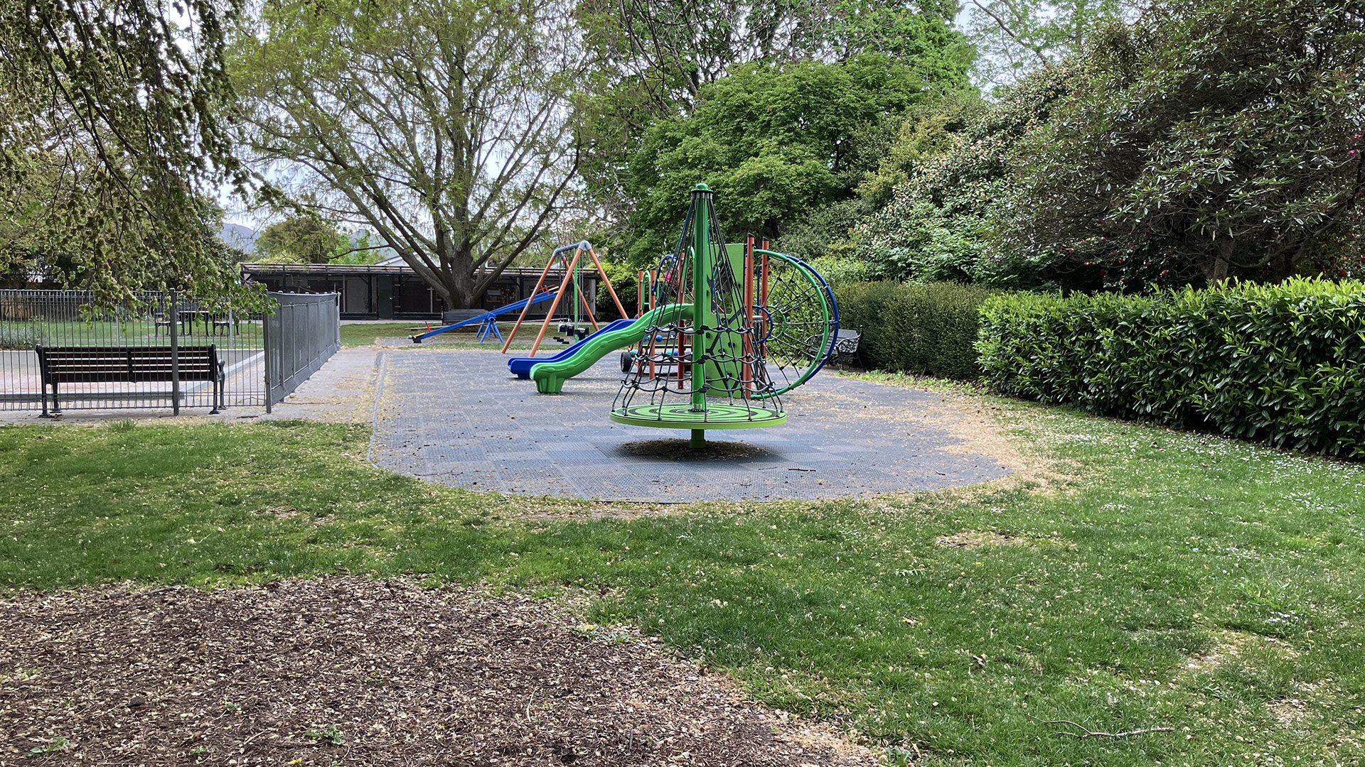 Park lawn with playground equipment and mature trees