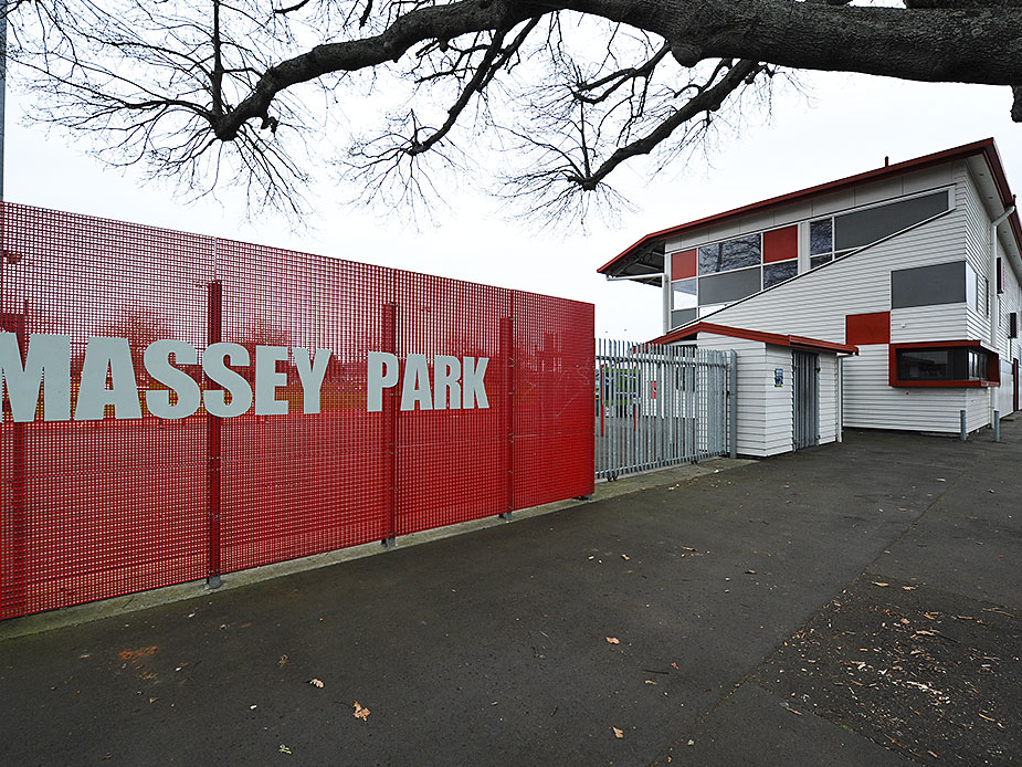 Park grandstand exterior with red signage fence and two-storey white weatherboard building