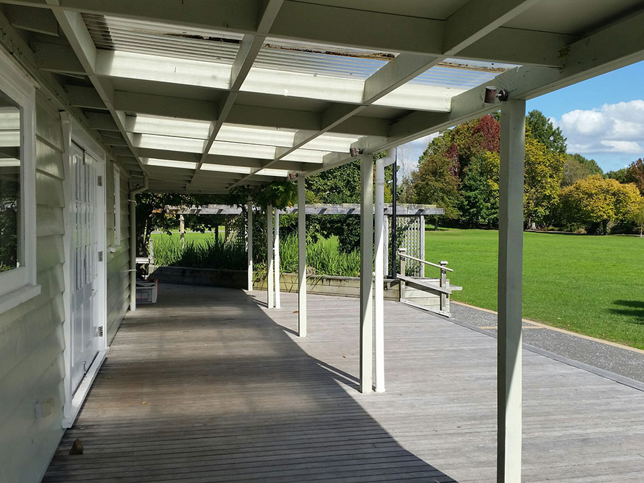 Covered deck walkway alongside building with green lawn beyond