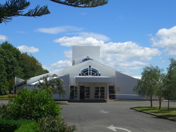 White modern church building with large arched entrance and surrounding trees