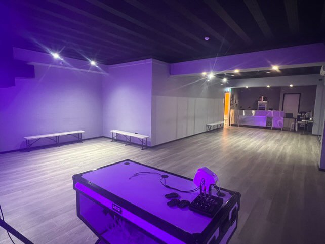 Open-plan room with timber flooring, purple uplighting, a DJ setup, and folding bench seating