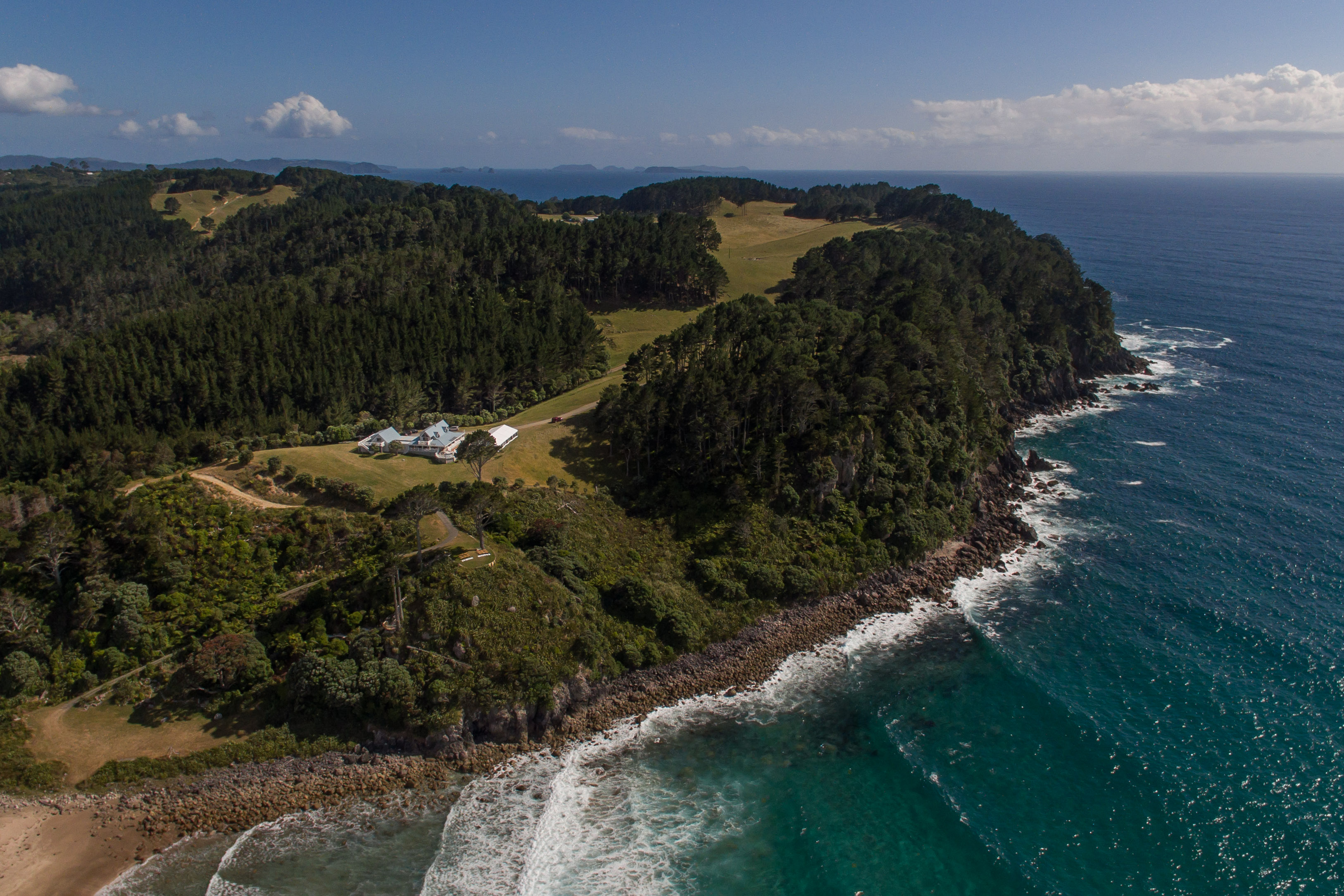 Aerial view of the headland property with buildings among trees above the coastline