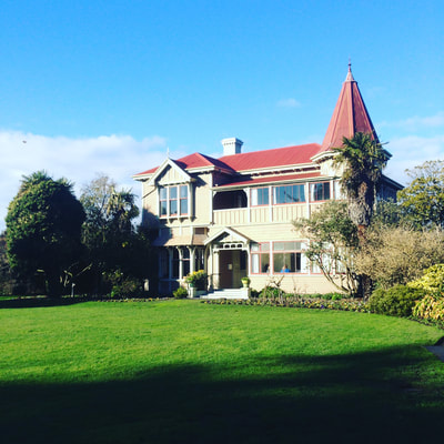 Two-storey heritage villa with red-roofed tower, set in a lawn with established trees