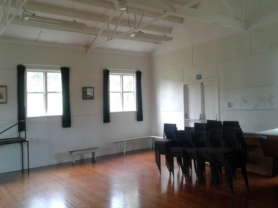 Plain white hall interior with timber floor and stacked chairs