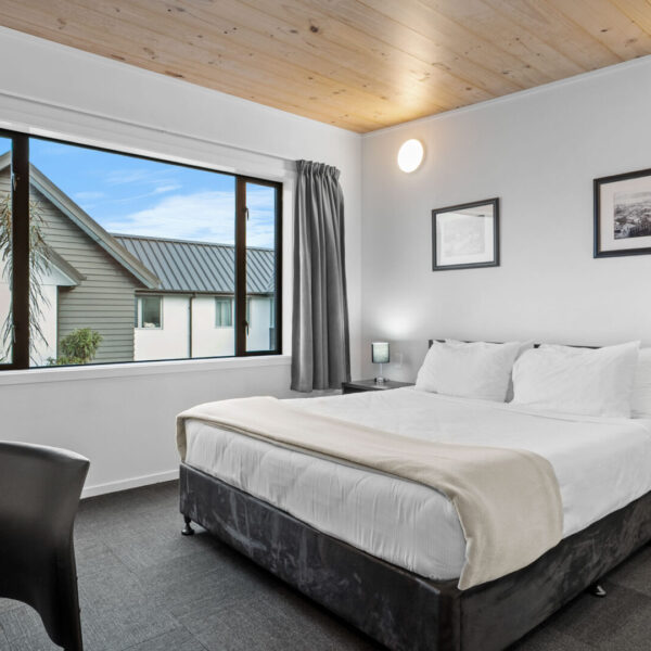 Simply furnished hotel bedroom with timber ceiling and garden view
