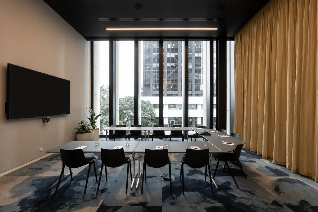 Compact meeting room with rectangular table, dark chairs, floor-to-ceiling windows with city views and gold curtain