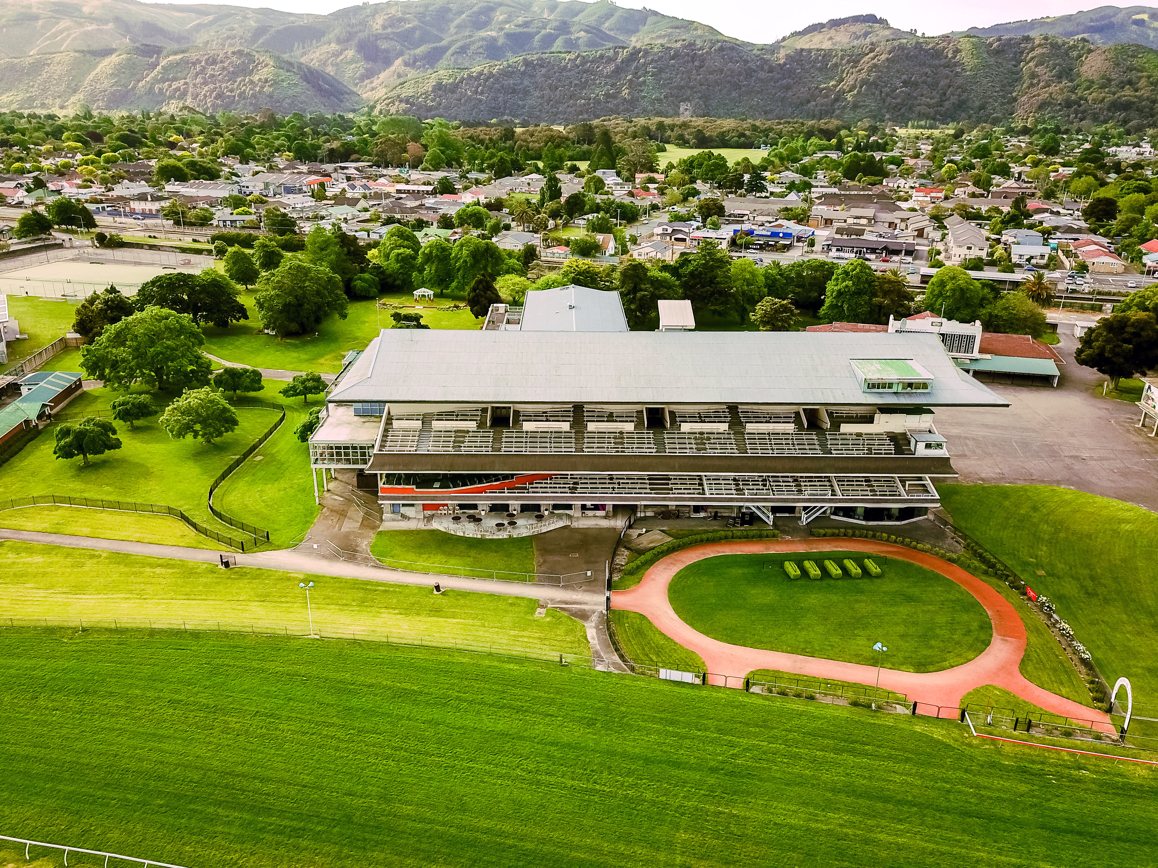 Aerial view of multi-level grandstand building at racecourse with green lawns and hills beyond