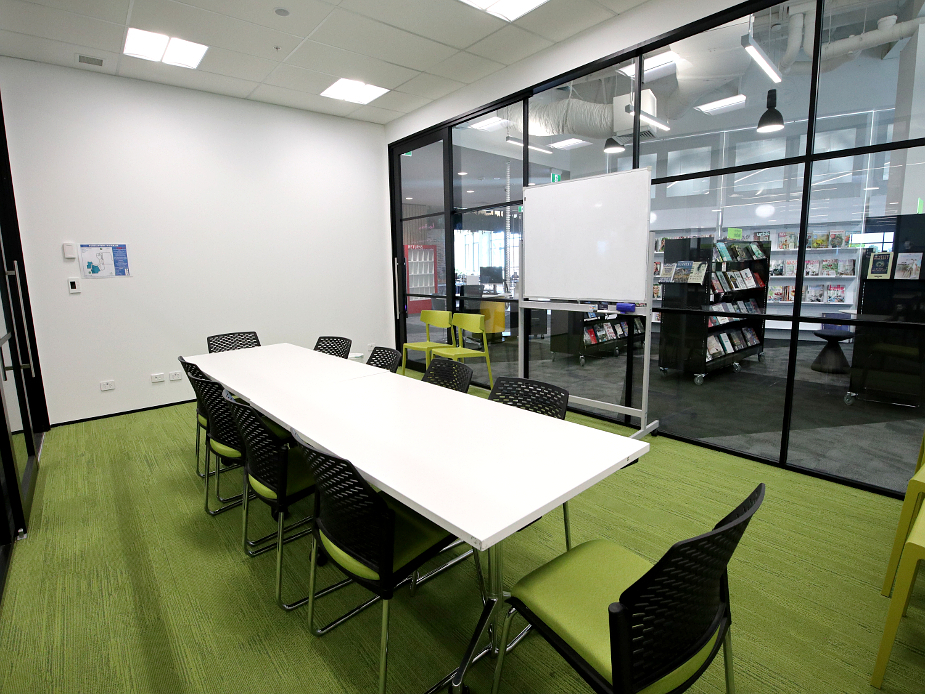 Meeting room with long table, green chairs, whiteboard, and glass wall