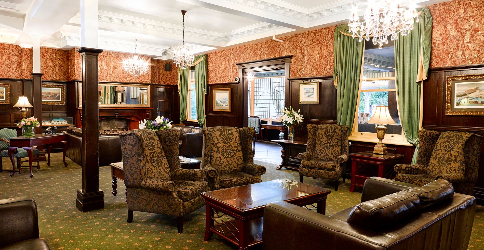 Heritage lounge with patterned armchairs, dark timber columns, crystal chandeliers and decorative wallpaper