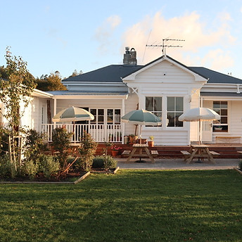 White timber cottage exterior with verandah, outdoor tables and umbrellas, small lawn garden