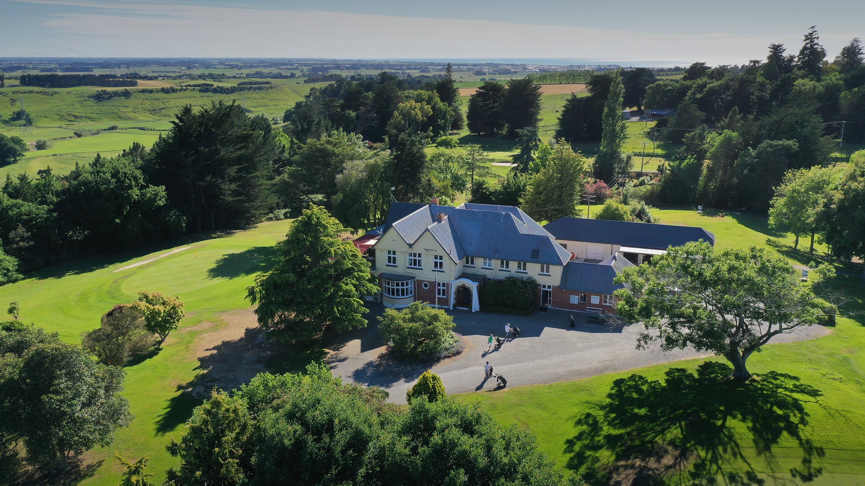Aerial view of golf clubhouse and grounds amid trees and fairways