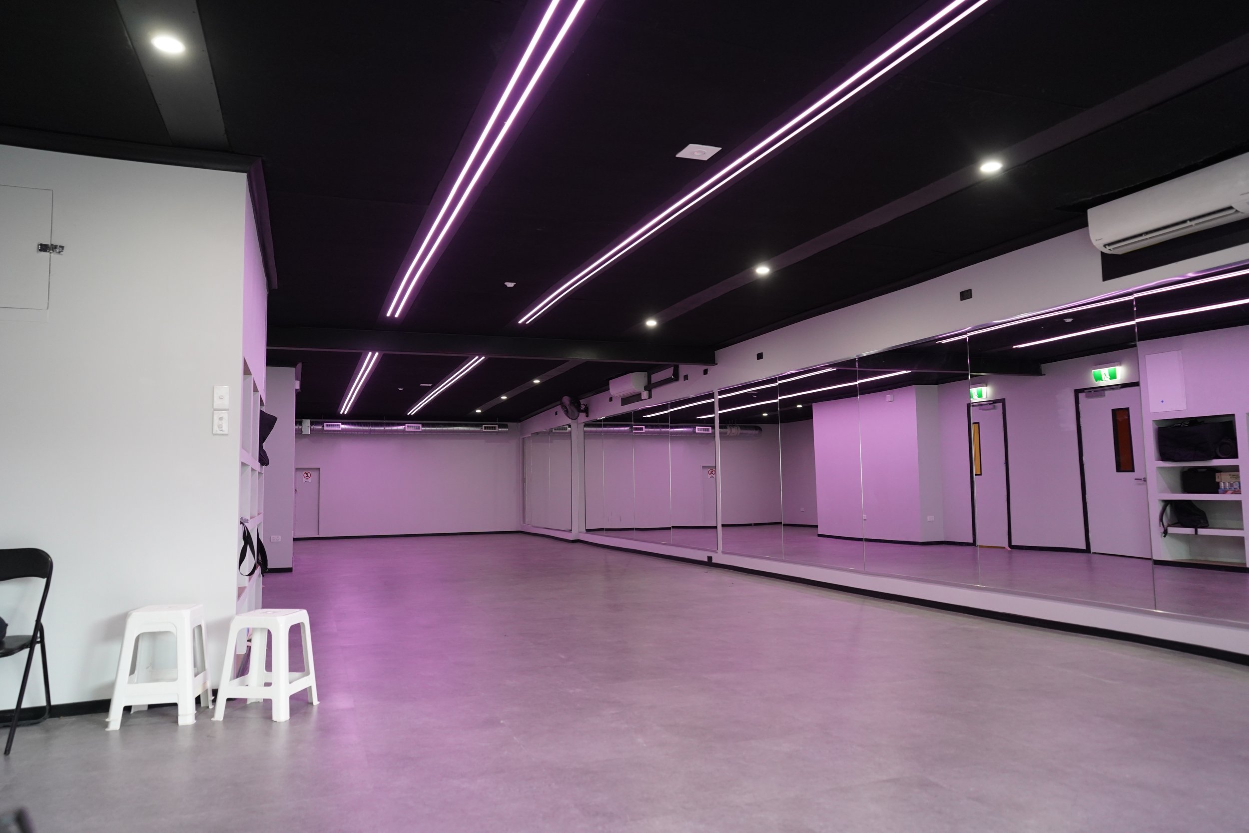 Bare concrete-floored studio with black ceiling, strip LED lighting, and a mirrored wall