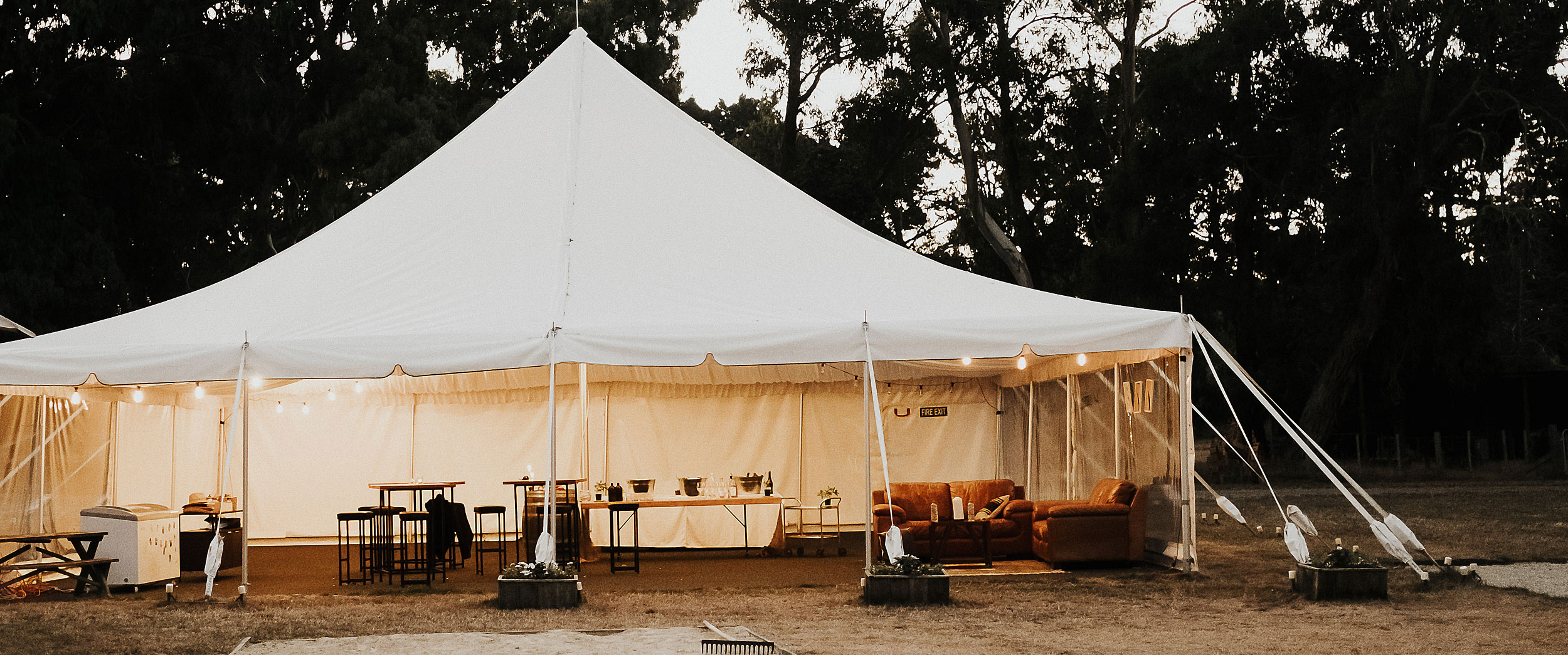 White marquee tent set up on farm grounds at dusk with festoon lights