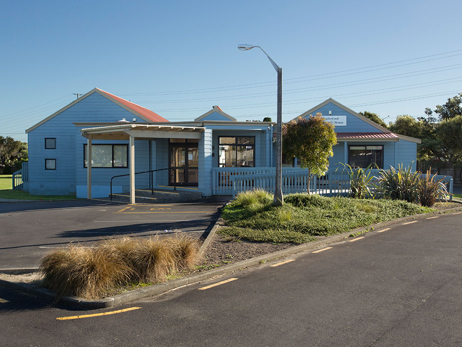 Blue weatherboard community house building with covered entry and plantings