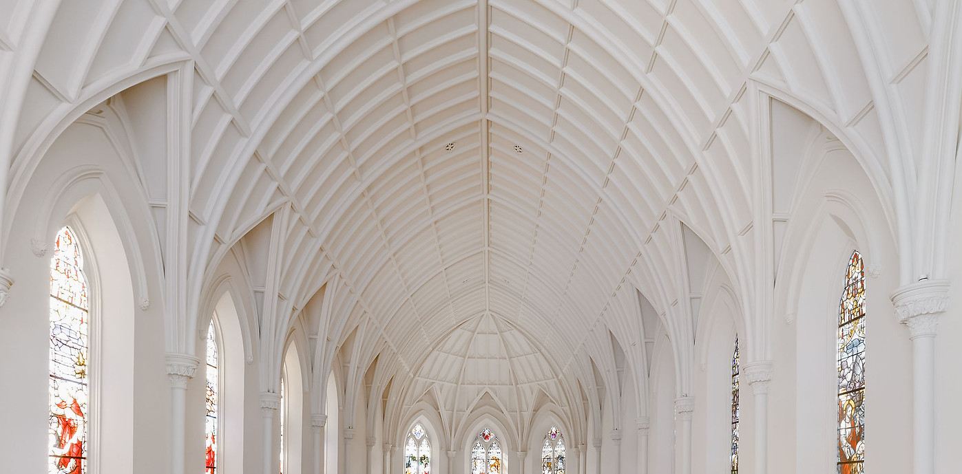 White chapel interior with high vaulted Gothic arches and stained glass windows