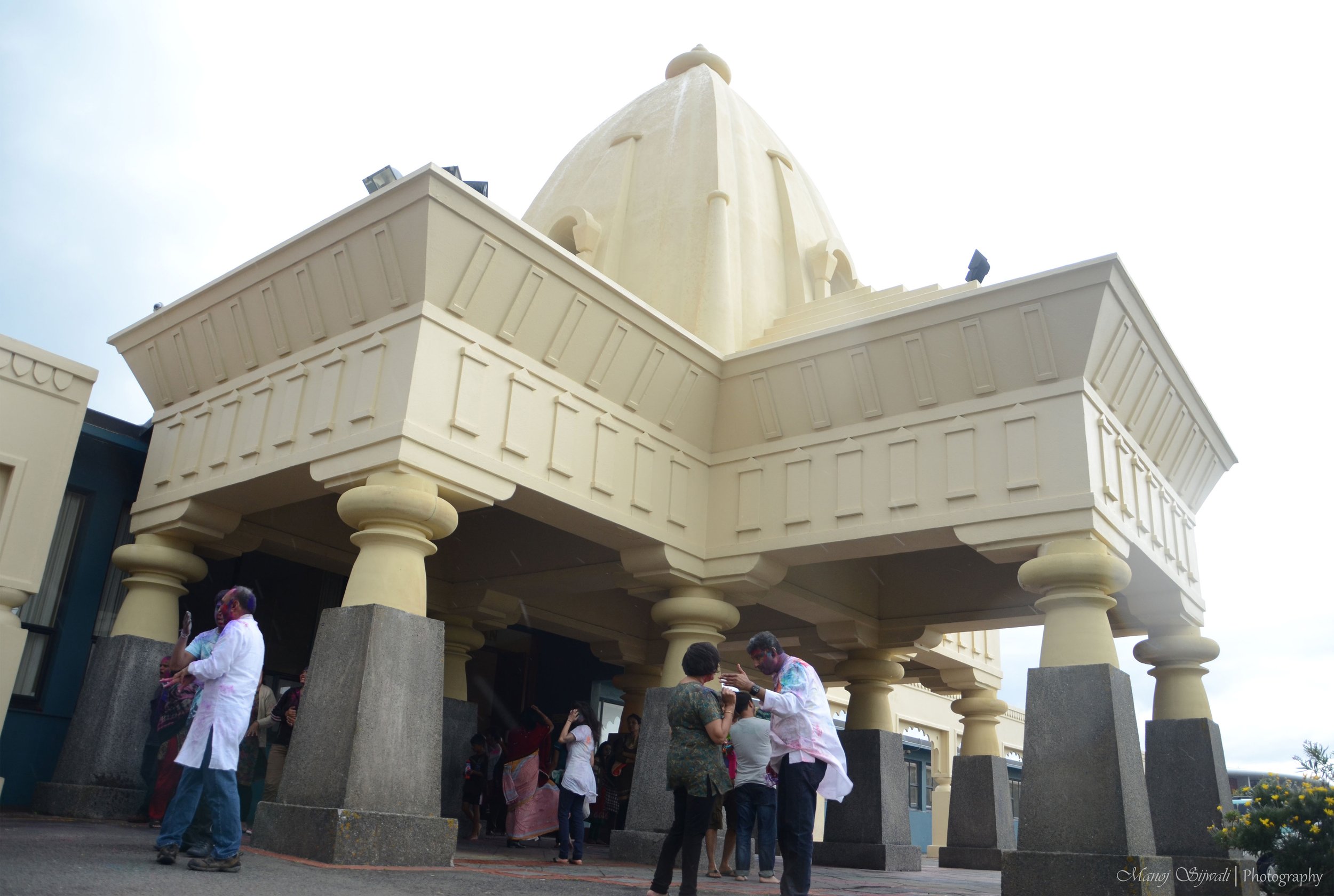 Ornate building entrance with columns and a dome structure, people gathered at the door