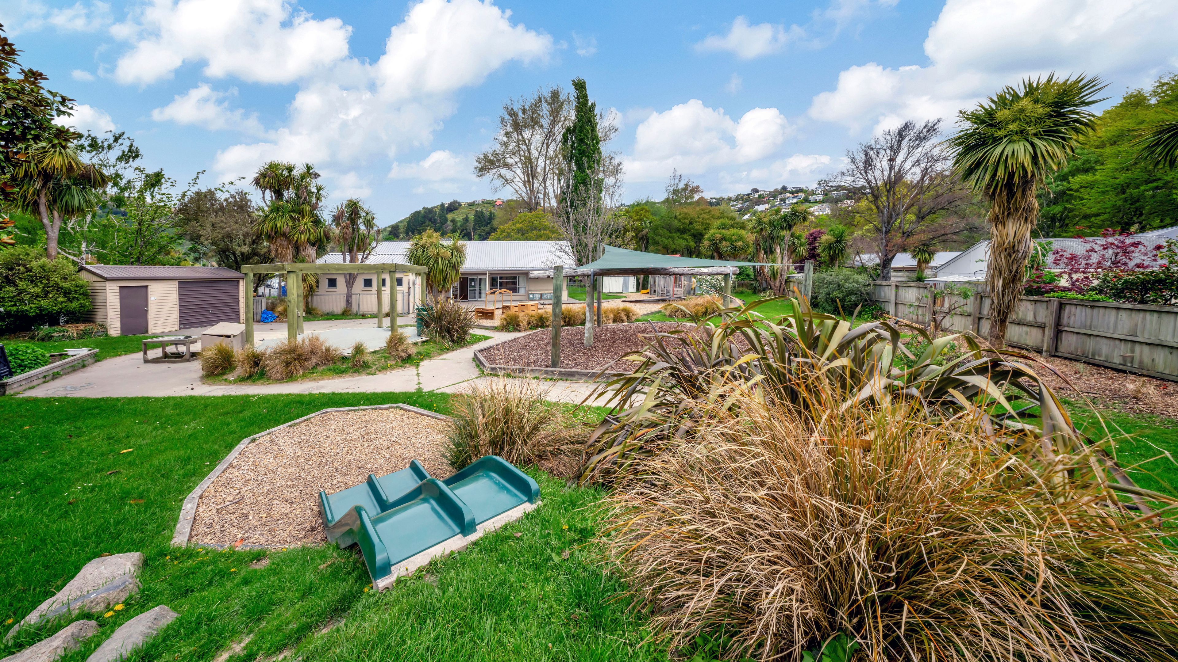 Outdoor grounds with garden beds, trees and small playground equipment