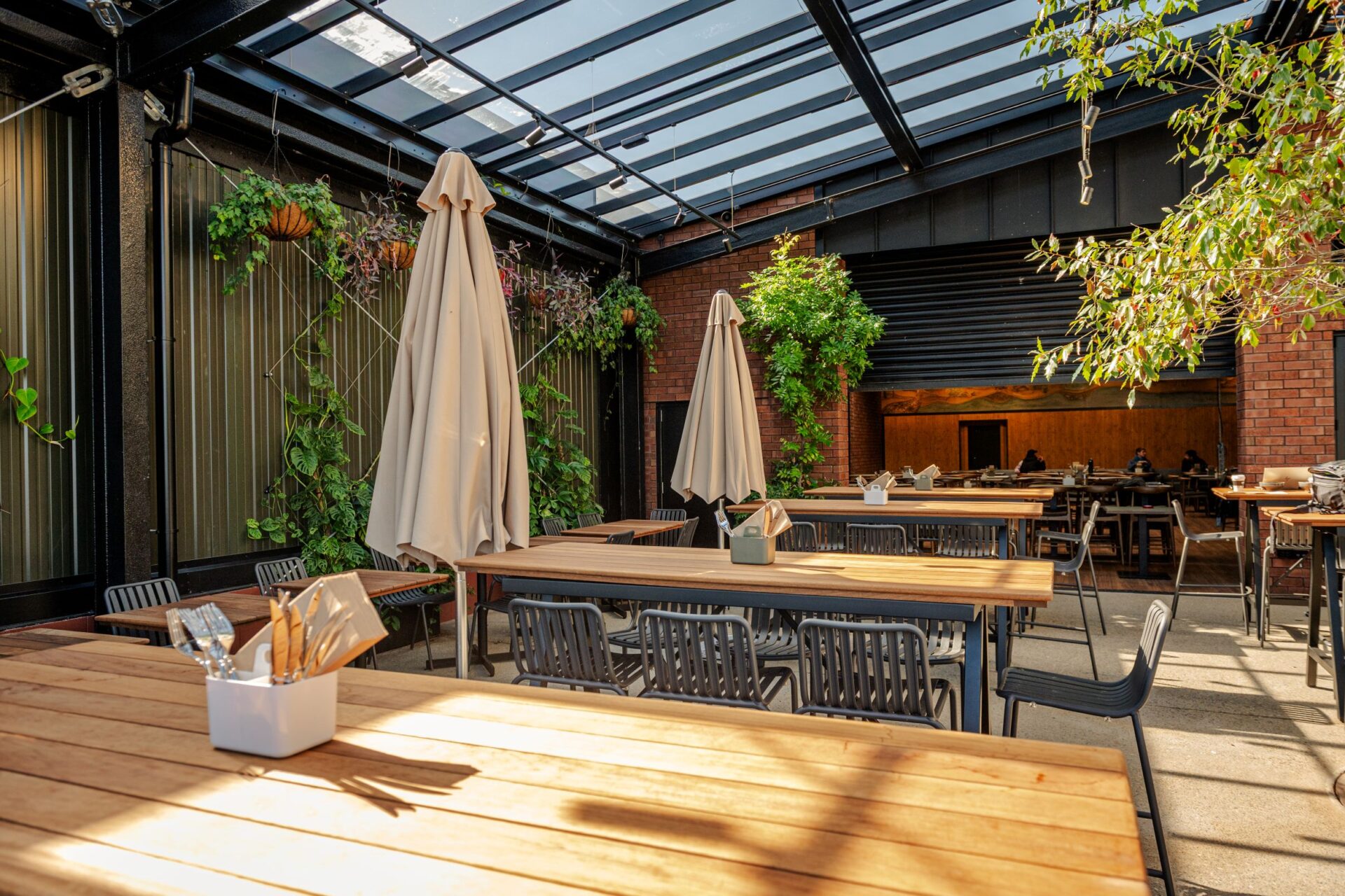 Glass-roofed courtyard with timber tables, hanging plants and brick wall, set for dining