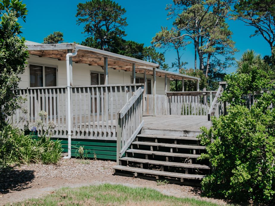 Small weatherboard hall with veranda, steps and surrounding planting