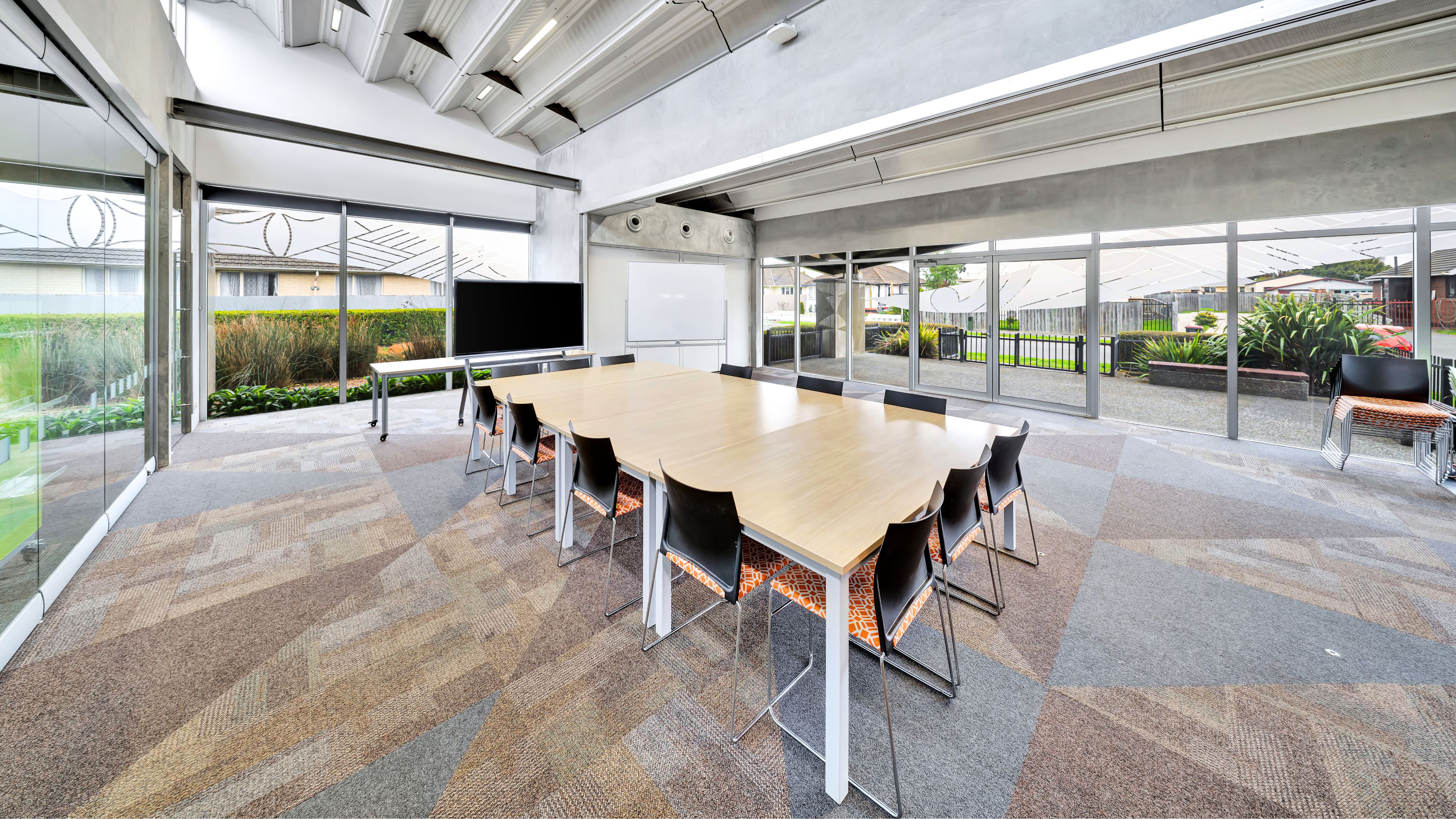 Boardroom with long table, wall-mounted screen, floor-to-ceiling glazing to outdoor area