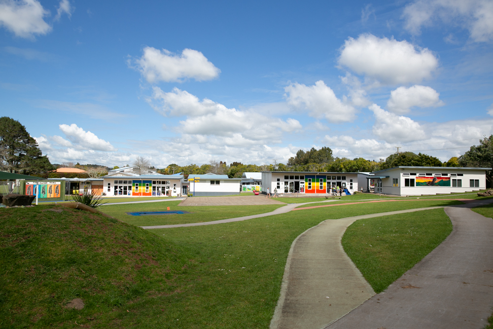 School buildings and playground on open lawn under blue sky