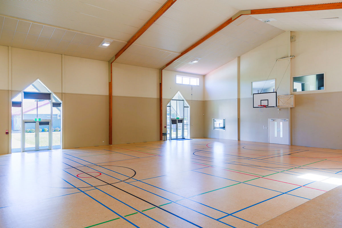 Sports hall interior with court markings, high ceiling, and basketball backboard on far wall