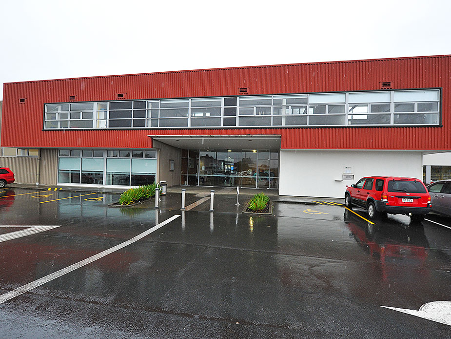 Red corrugated building with strip windows and car park in rain