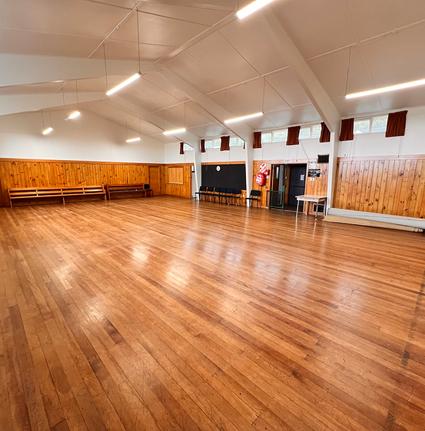 Open timber-floored hall with pine-lined walls, vaulted ceiling, and fluorescent strip lighting