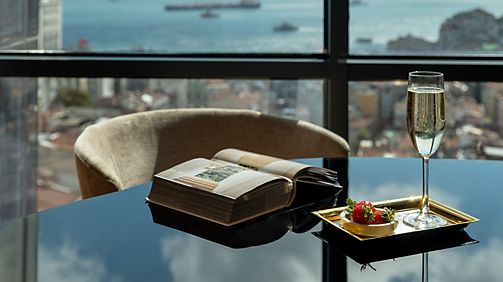 Glossy dark table with champagne glass, book, and small dish beside a panoramic city view
