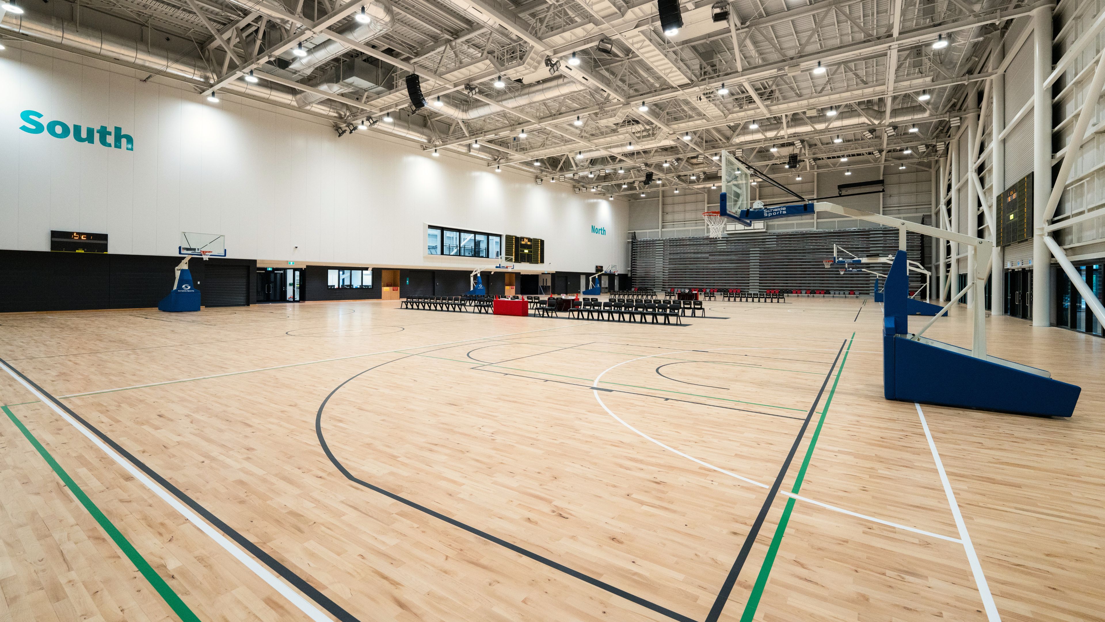 Large indoor sports hall with timber court markings, high ceiling, roof trusses and retractable seating