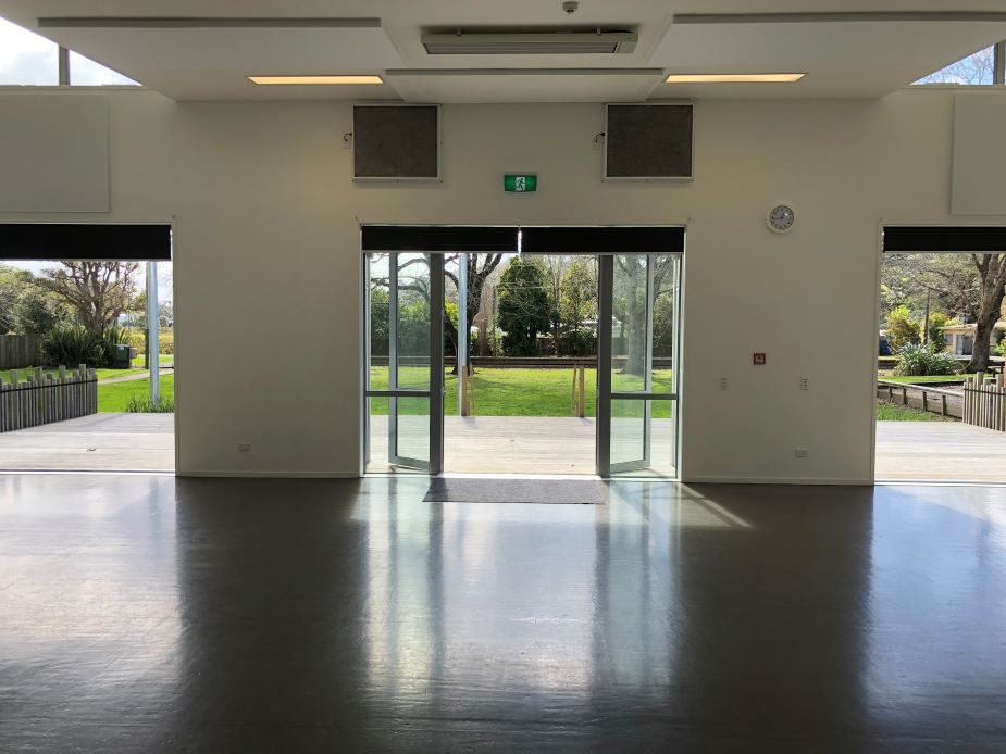 White-walled hall interior with polished dark floor, glass sliding doors opening to a lawned reserve