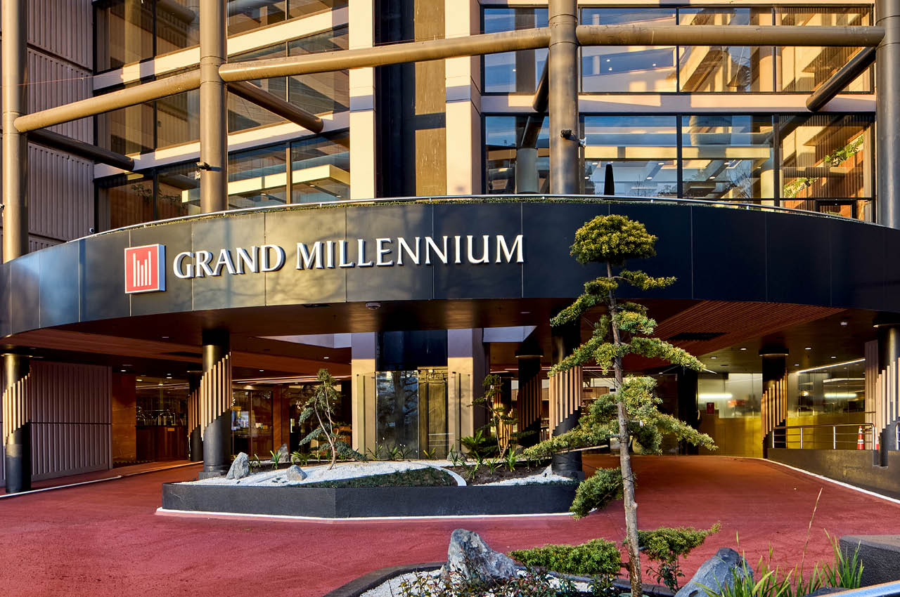 Grand Millennium hotel entrance with curved canopy, timber accents, and sculpted trees