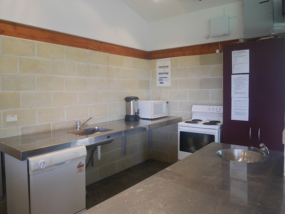 Hall kitchen with bench, stove, microwave and block-wall splashback