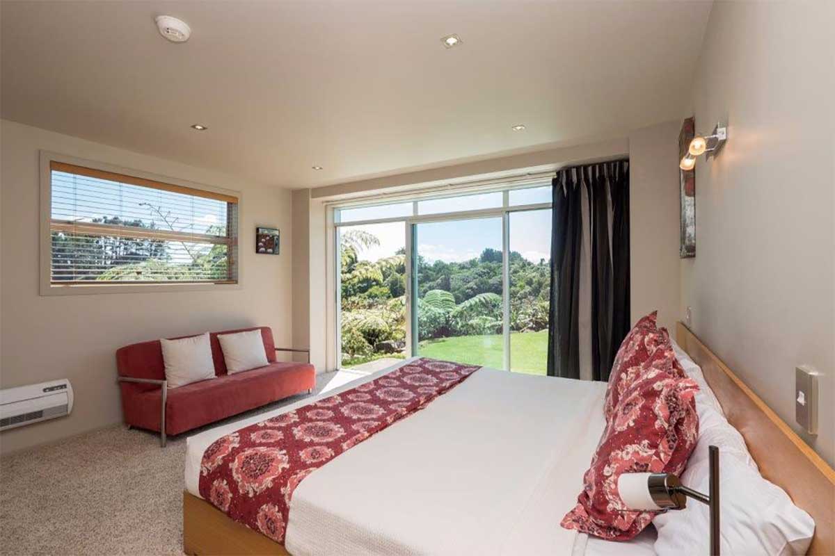 Studio with a king bed, red sofa and sliding doors opening to a garden view