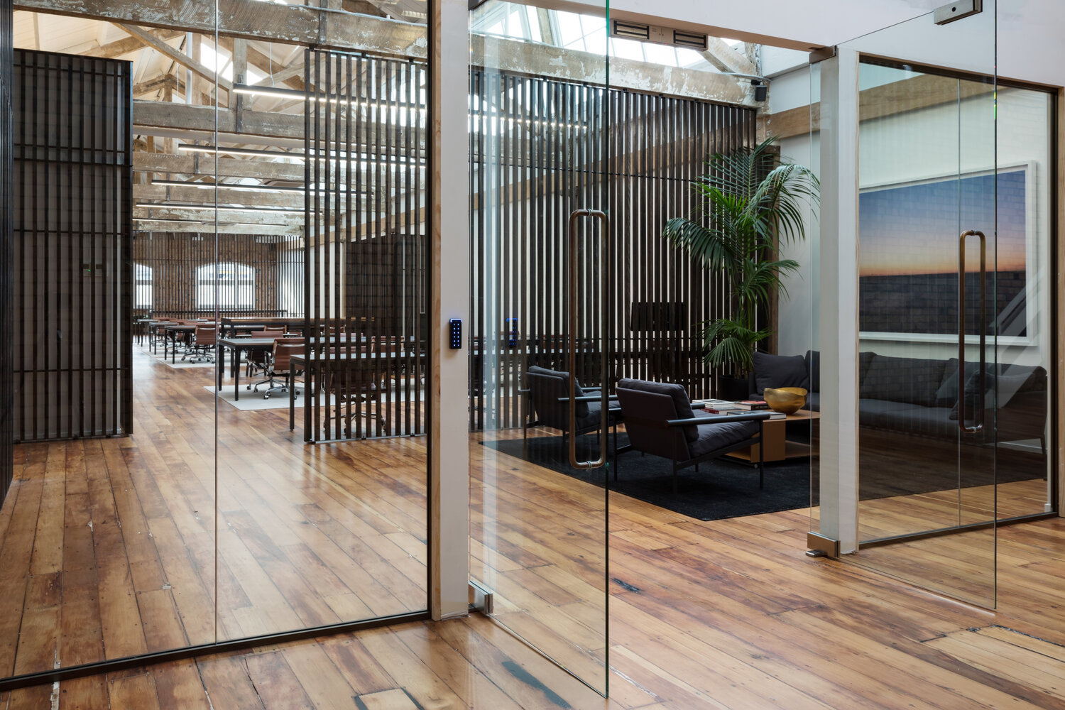 Open-plan loft space with timber floor, vertical slat screens, glass-walled meeting rooms