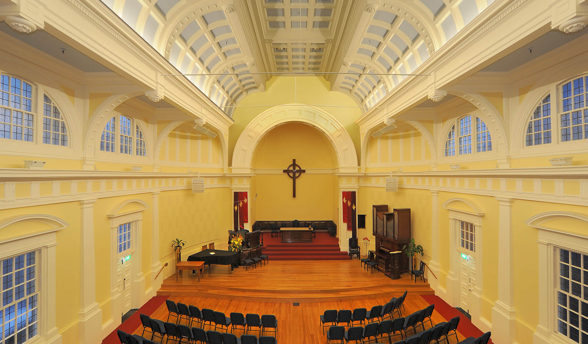 Pale yellow church interior viewed from above showing arched apse, wooden cross, and rows of chairs