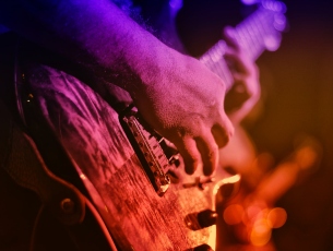Close-up of hands playing electric guitar under coloured stage lighting