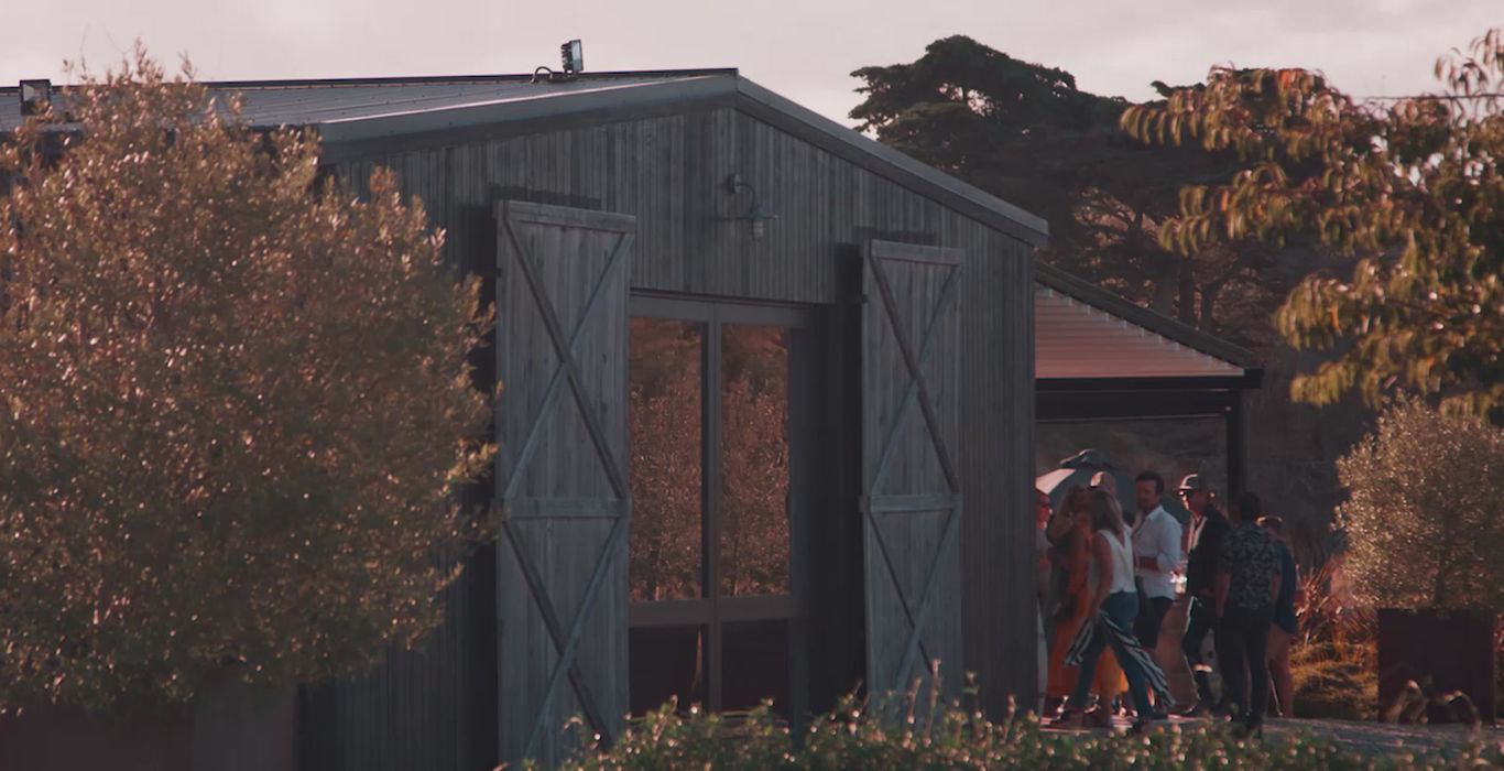 Dark timber clad barn building with large doors, surrounded by trees at golden hour