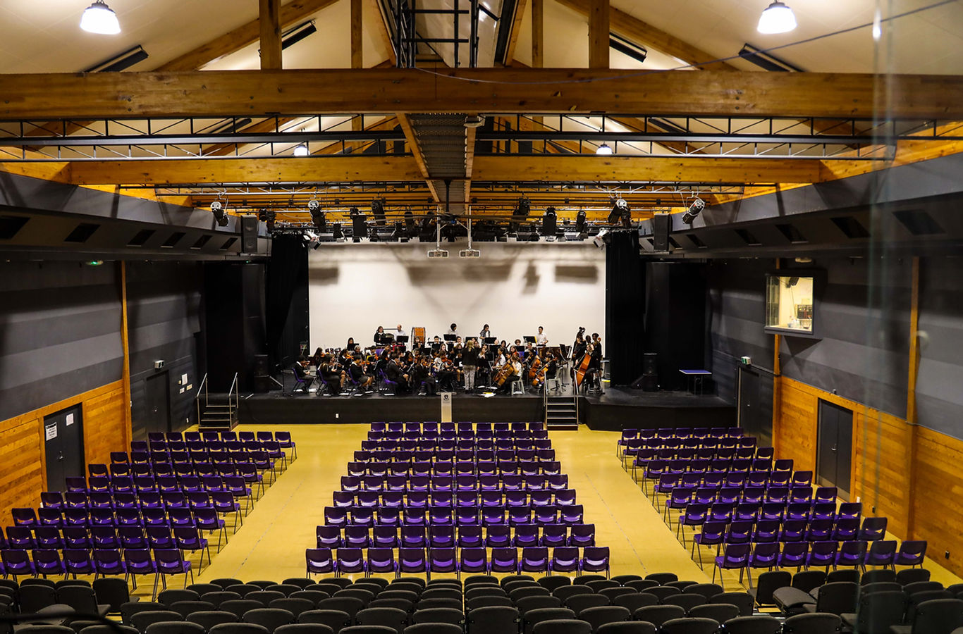Timber-framed performing arts hall with rows of purple seats and an orchestra on stage