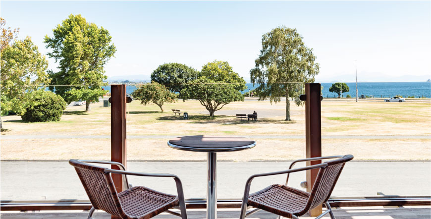 Balcony terrace with two rattan chairs and round table, overlooking park and lake