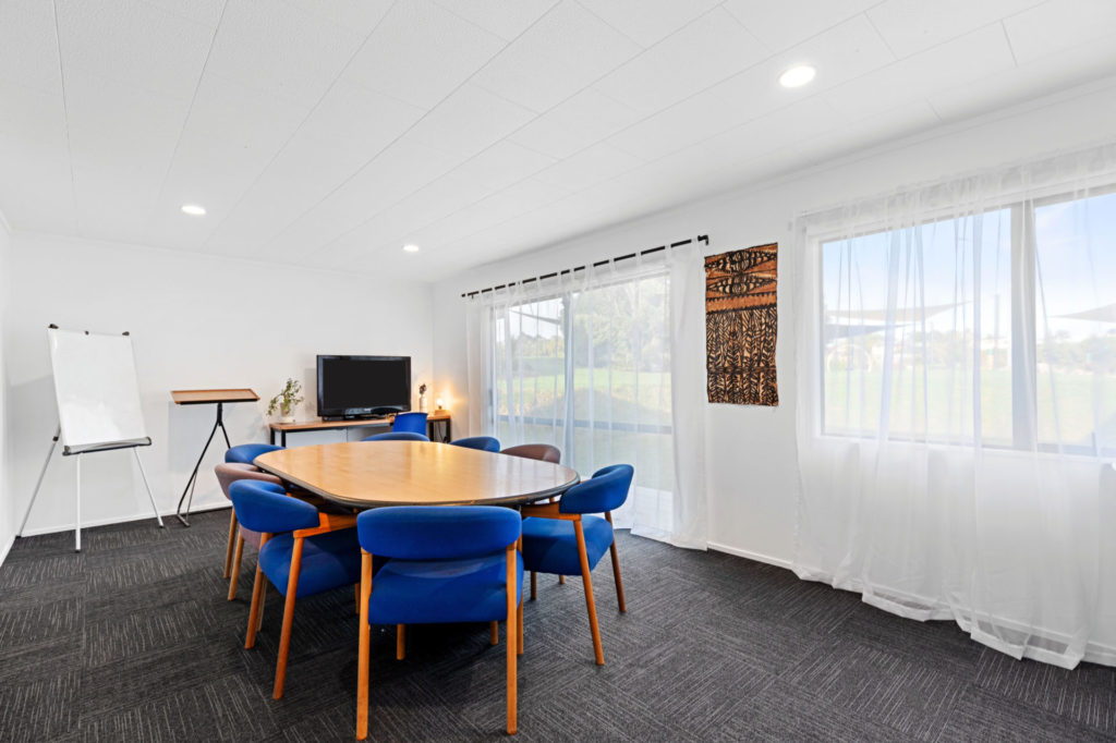 Meeting room with oval table, blue chairs, whiteboard, and large windows