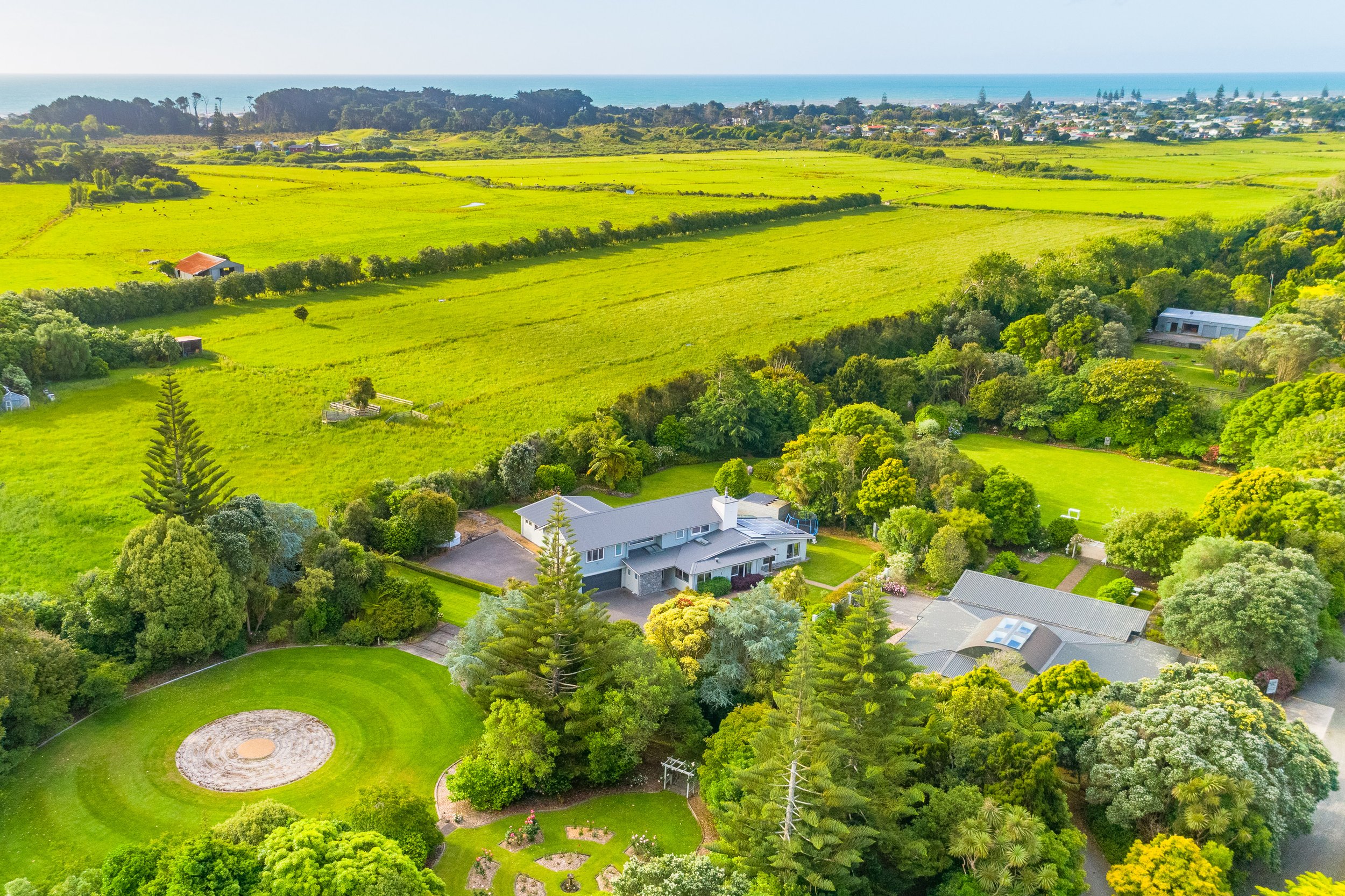 Aerial view of house and grounds surrounded by trees and farmland with coast in background