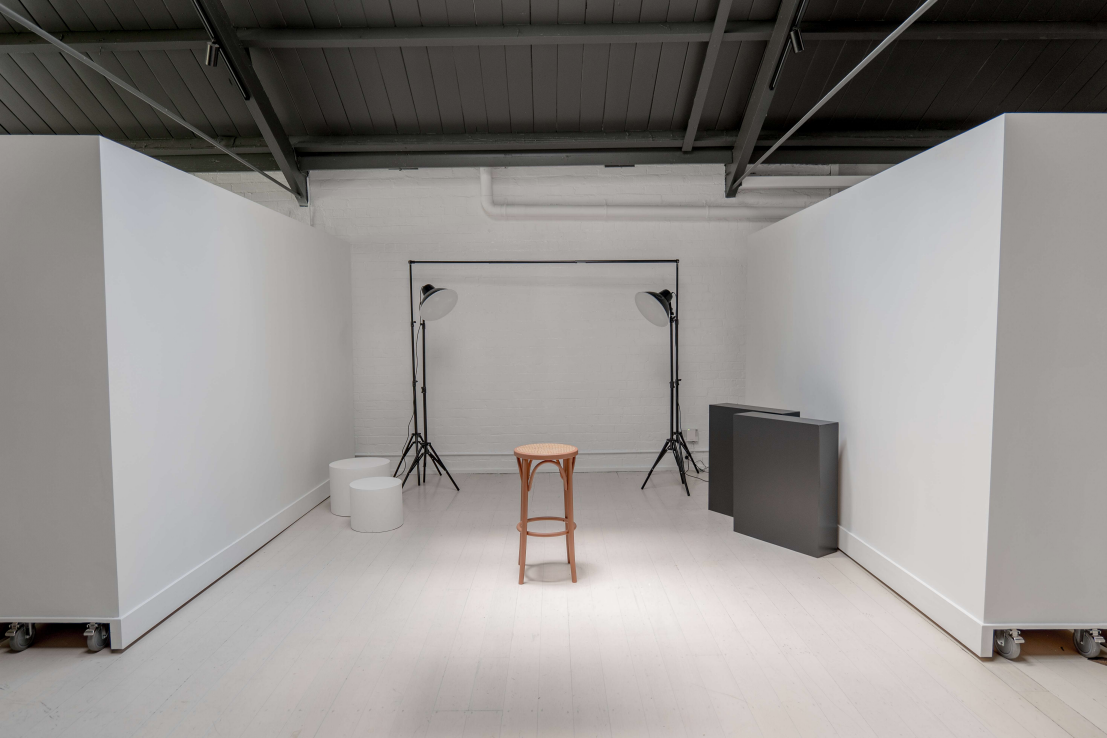 White photography studio with movable white panels, two studio lights, and a single stool