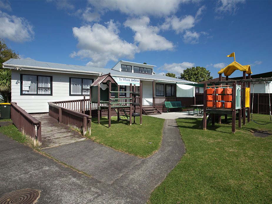 Single-storey white weatherboard community building with playground and garden